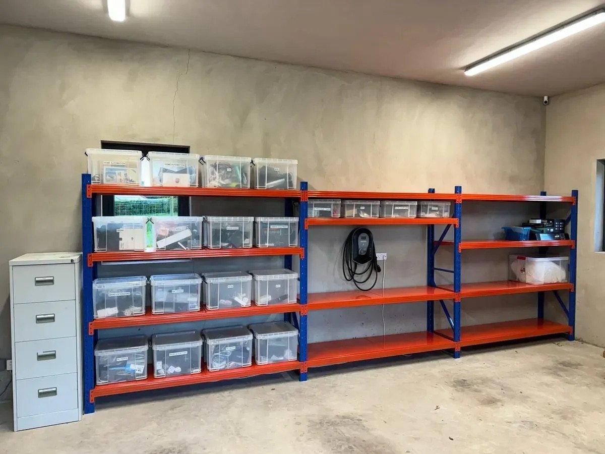 Garage con estanterías naranja y azul armadas en fila contra la pared, con cajas organizadoras